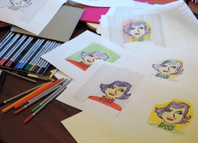 Photo of coloring pencils on a desk, with versions of the Absolutely Maybe cartoon logo testing out different colors (by Hilda Bastian)